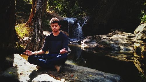 Full length of young man meditating on rock in forest