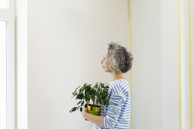 Woman with potted plant standing in front of white wall at new home