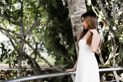 Side view of young woman standing against trees