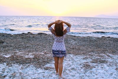 Rear view of woman standing at beach against sky during sunset