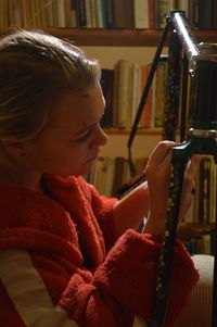 Woman painting bicycle frame against bookshelf