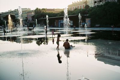 Reflection of men on lake in city