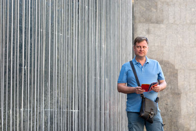 Portrait of man holding camera while standing against wall