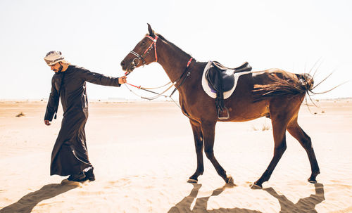 Man with horse walking in desert