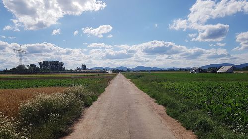 Dirt road amidst field against sky