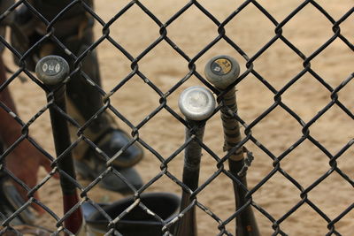 High angle view of baseball bats leaning on chainlink fence