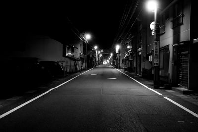 Empty road along illuminated buildings at night