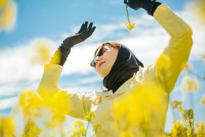Low angle view portrait of a stylish woman among a blooming yellow field under a bright spring sky