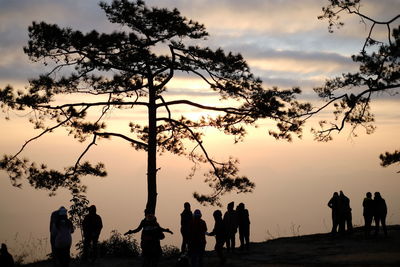 Silhouette people by trees against sky during sunset