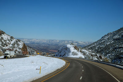 Road amidst snowcapped mountains against clear sky during winter