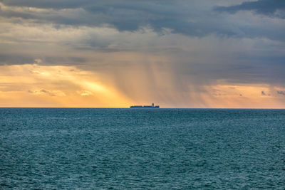Dramatic cloudy sky and sun shining over sea with cargo ship sailing far away from coast, raining