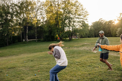 Female counselor avoiding splash of water while playing on grass with friends at summer camp