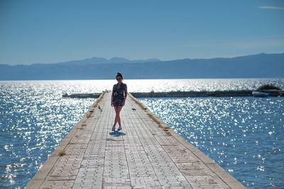 Rear view of woman walking at beach against sky