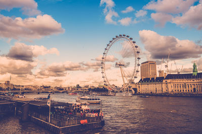 Ferris wheel in city against cloudy sky