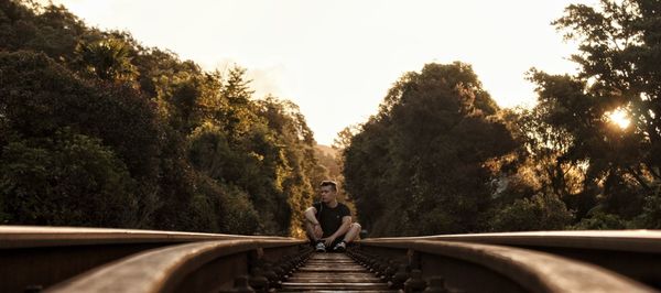 Young man sitting on railroad track against clear sky