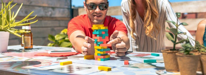 Concentrated young man pushing jenga game piece next to female friend in rooftop party