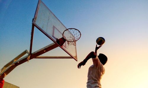 Side view of man throwing basketball in hoop against clear sky