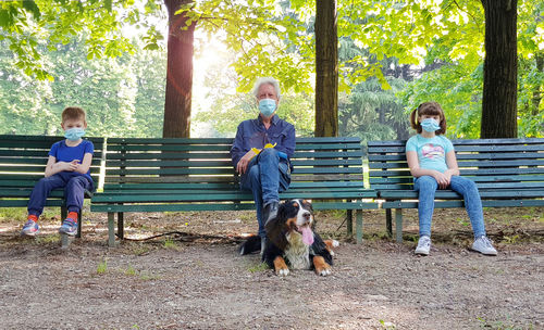 Full length of grandfather with grandchildren sitting on bench at park