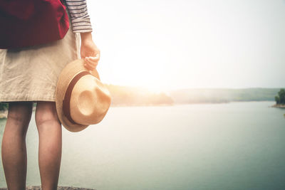 Midsection of woman holding umbrella standing by sea against sky