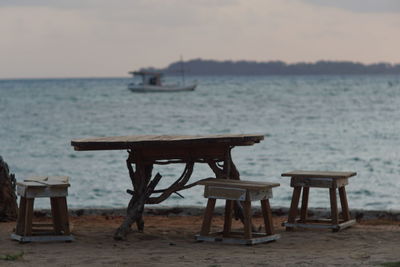 Empty chairs and table at beach against sky