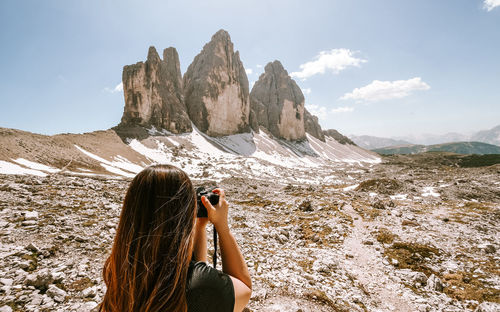 Woman photographing rock on mountain against sky