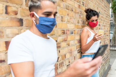 Portrait of young man using mobile phone against wall