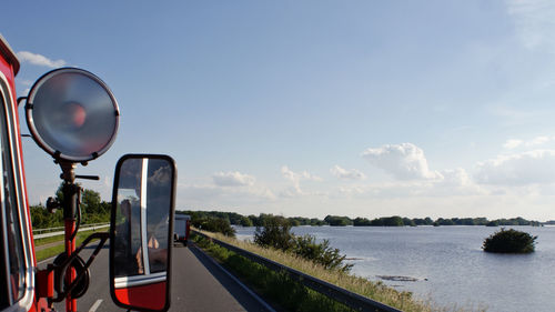 Cars on road by river against sky