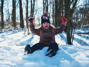 Portrait of little girl smiling sitting in snow. full length. looking at camera.