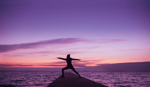 Silhouette woman standing pier by sea against sky during sunset