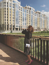 Rear view of woman standing by railing against buildings in city