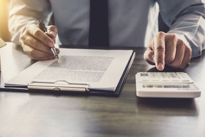 Midsection of man using calculator at desk