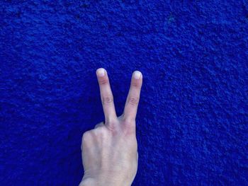 Cropped image of hand gesturing peace sign against blue wall