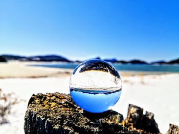 Close-up of crystal ball on rocks against clear blue sky
