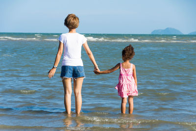 Rear view of siblings standing at beach against clear sky