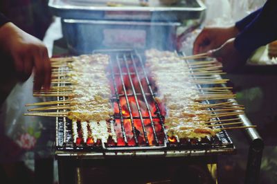 Cropped hands of vendors preparing food on barbecue grill