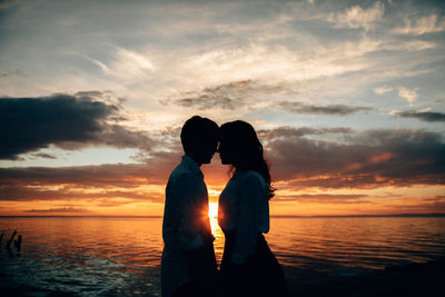 Silhouette couple standing by sea against sky during sunset