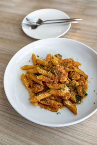 Spicy italian sausage penne in a round white plate, empty plate with cutlery, on a wood grain table