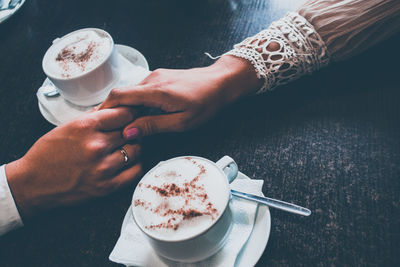 Cropped image of couple holding hands by coffee cups on table