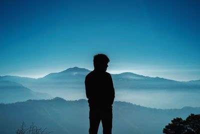 Silhouette man looking at mountains against blue sky