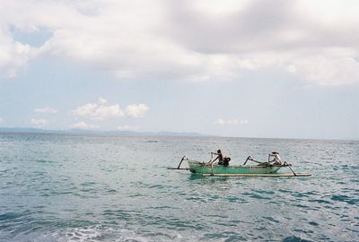 Men in sailing boat on sea against sky