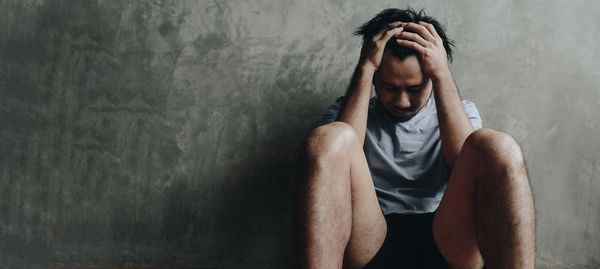 Portrait of young man sitting against wall