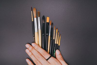 Close-up of hand holding pencils against colored background