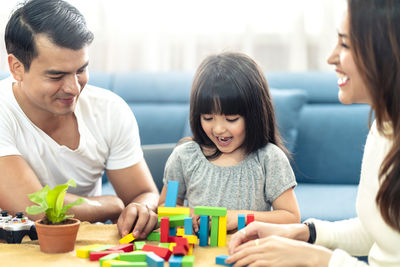 Happy parents with daughter stacking toy blocks on table at home