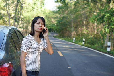 Beautiful young woman sitting on road against trees