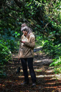 Woman using smart phone while standing amidst trees in forest