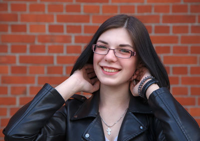 Portrait of smiling young woman against brick wall