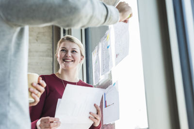 Two smiling colleagues with papers at office window