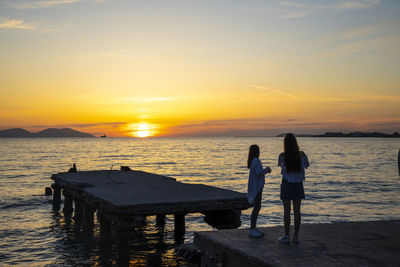 Rear view of women standing at beach during sunset