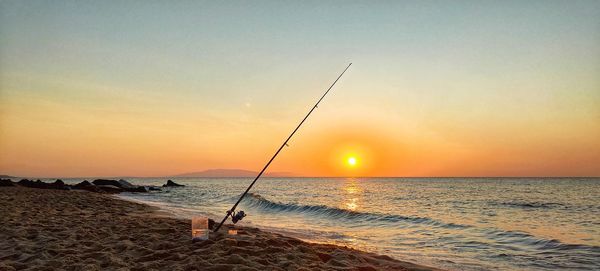 Fishing rod on beach against sky during sunset