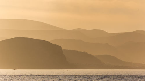 Scenic view of sea and silhouette mountains against sky